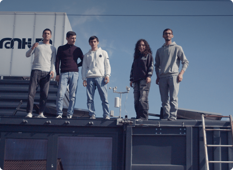 A group of young poeple standing on a building with the blue sky behind them