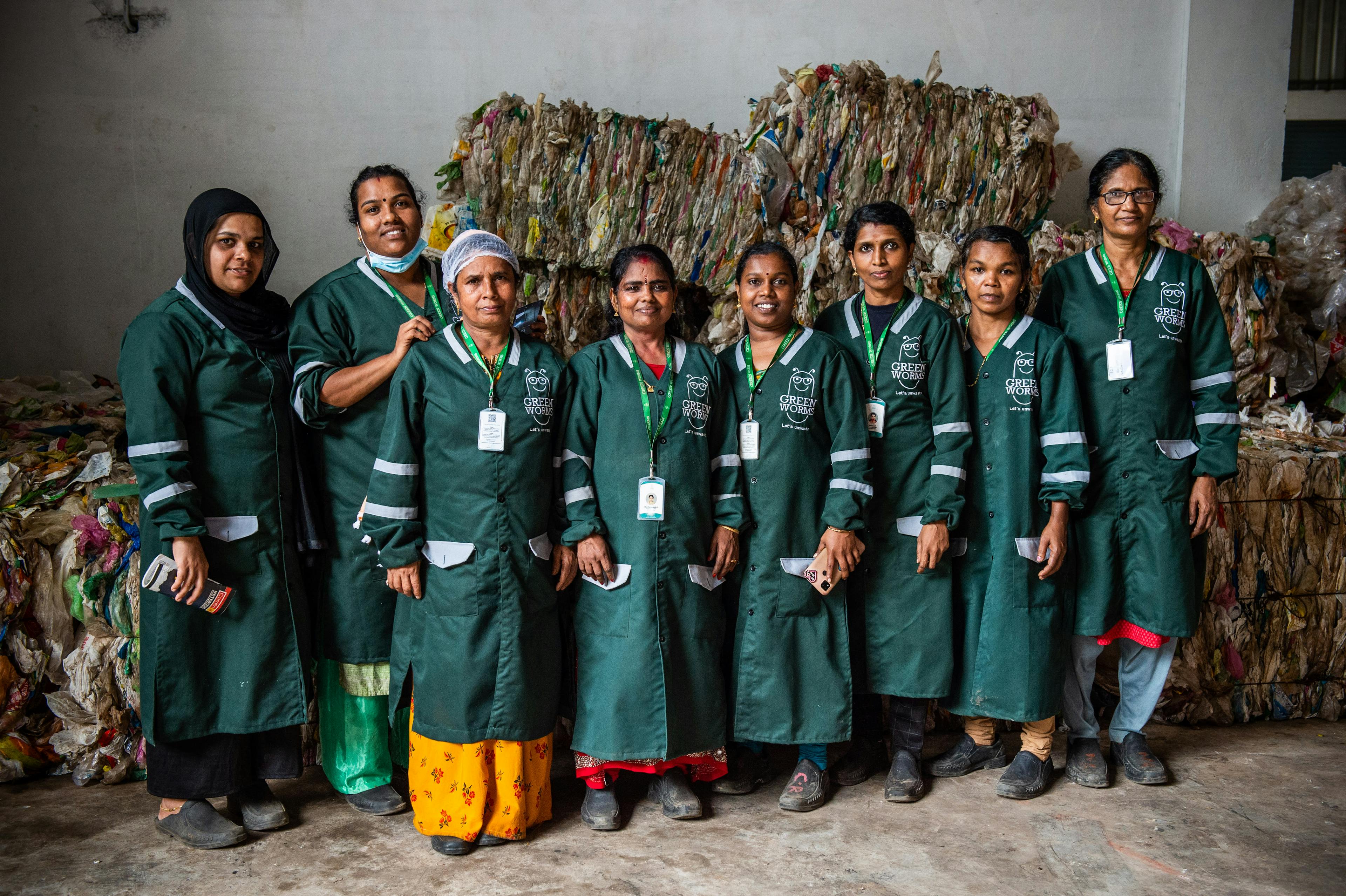 A lineup of women wearing the green rePurpose uniform, standing shoulder to shoulder. Behind them, a pile of sorted waste ready to be repurposed.