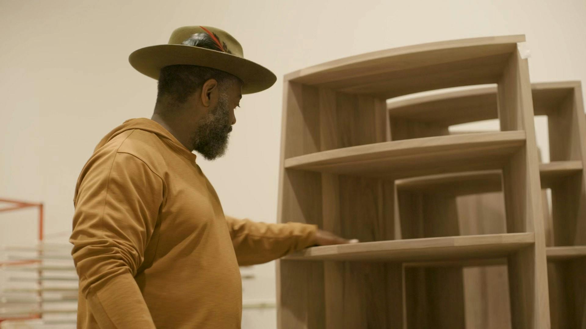 Dwayne Betts wearing a hat and touching a wooden shelf.