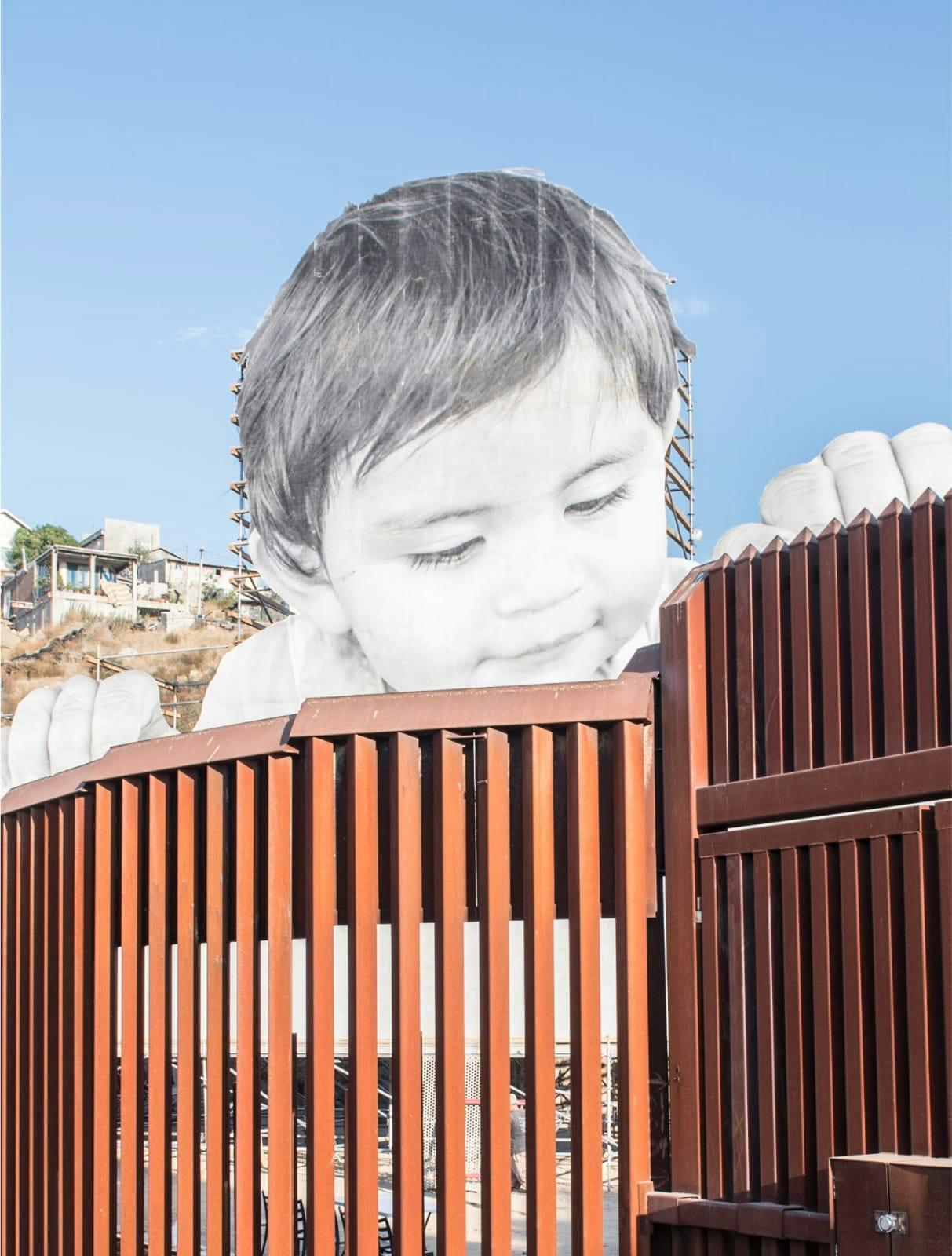 Image of a border wall with a mural of a large sized child looking over it