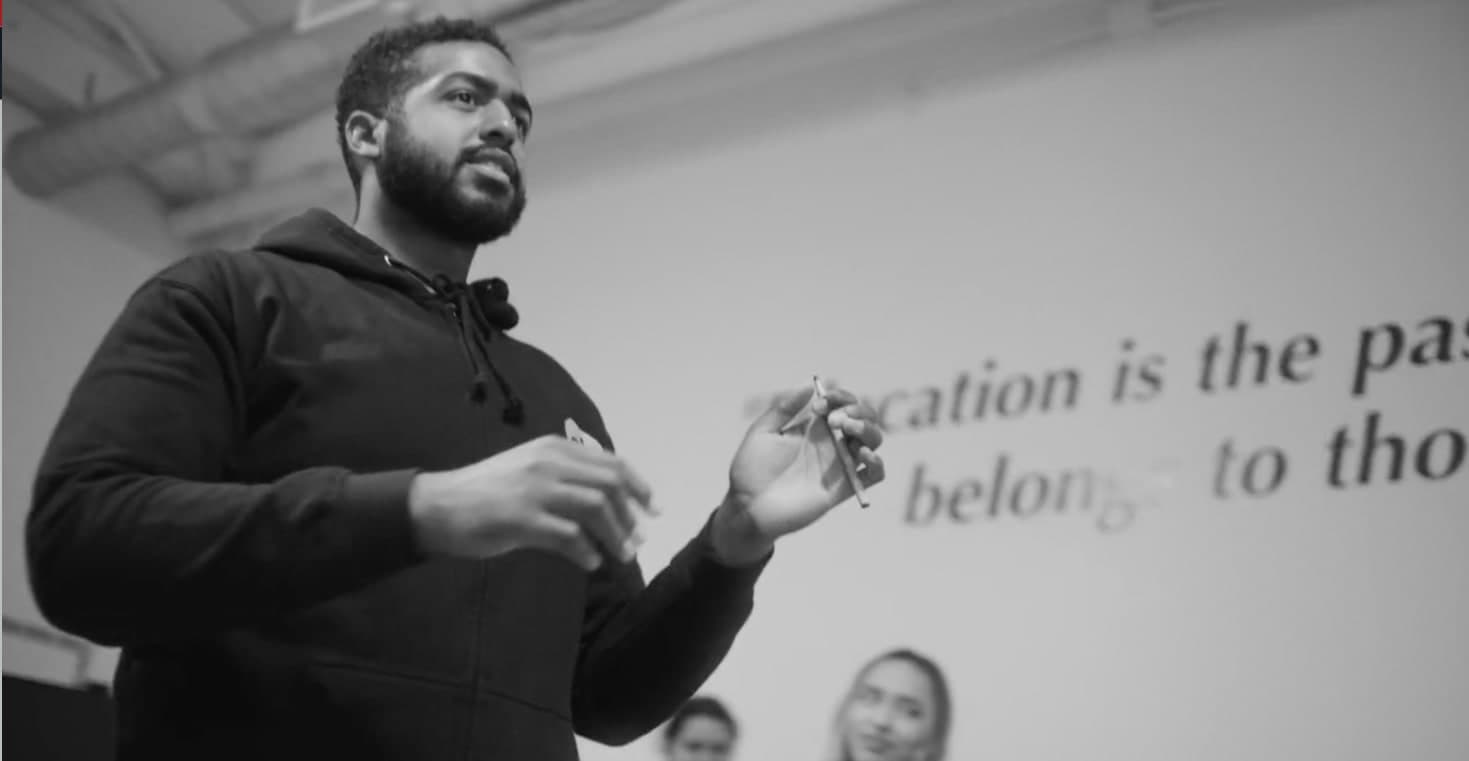 A man wearing a black sweater gesturing as he speaks taken from the bottom angle