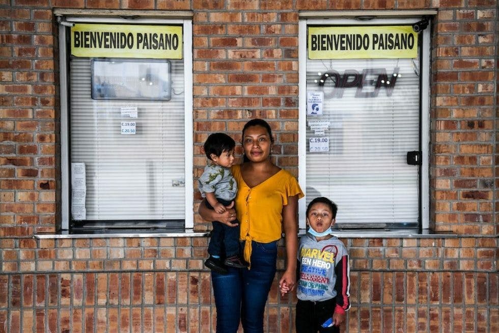 Mom and two sons in front of two windows with Bienvenido Paisano signs