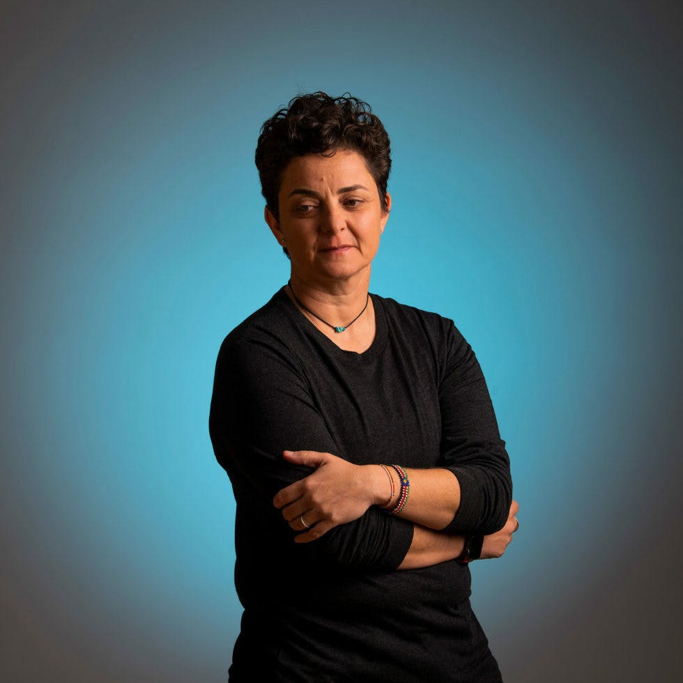 Picture of Mufleh with arms crossed, wearing all black with a gradient blue background.